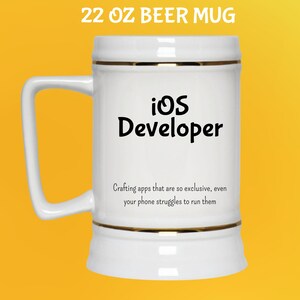 May include: White 650 ml beer mug with gold trim and a large handle. The mug features the text "iOS Developer" in black, and a humorous quote about app development. The mug is set against a yellow background.