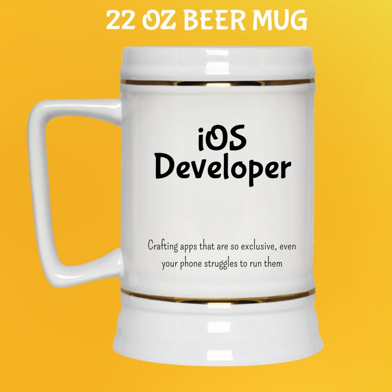 May include: White 650 ml beer mug with gold trim and a large handle. The mug features the text "iOS Developer" in black, and a humorous quote about app development. The mug is set against a yellow background.