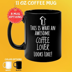 Op de afbeelding: Zwarte koffiemok van 325 ml met de tekst "THIS IS WHAT AN AWESOME COFFEE LOVER LOOKS LIKE!". De mok heeft een zwart oor en de afbeelding toont witte en zwarte kleuropties.
