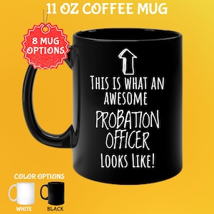 Op de afbeelding: Zwarte koffiemok van 325 ml met de tekst "THIS IS WHAT AN AWESOME PROBATION OFFICER LOOKS LIKE!" in het wit. De mok heeft een zwart handvat en een witte pijlgrafiek. Kleuropties zijn wit en zwart.
