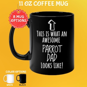 Può includere: Tazza da caffè nera da 325 ml con la scritta bianca "THIS IS WHAT AN AWESOME PARROT DAD LOOKS LIKE!". La tazza ha un manico nero e una grafica a freccia bianca. Le opzioni di colore includono tazze bianche e nere.