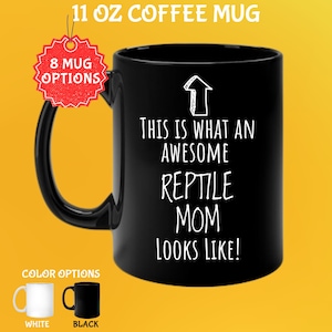 Puede incluir: Taza de café negra de 325 ml con el texto "THIS IS WHAT AN AWESOME REPTILE MOM LOOKS LIKE!" en blanco. La taza tiene un asa negra y un gráfico de flecha blanca. Las opciones de color incluyen blanco y negro.
