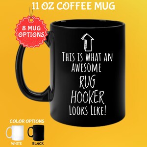 May include: Black 11 oz coffee mug with the text "THIS IS WHAT AN AWESOME RUG HOOKER LOOKS LIKE!" in white. The mug has a black handle and a white arrow graphic. Color options are white and black.