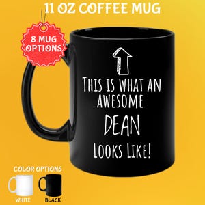May include: Black 11 oz coffee mug with the text "THIS IS WHAT AN AWESOME DEAN LOOKS LIKE!" in white. An arrow graphic is above the text. The mug has a black handle and is available in white and black.