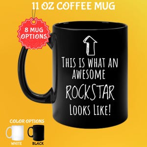 May include: Black 11 oz coffee mug with the text "THIS IS WHAT AN AWESOME ROCKSTAR LOOKS LIKE!" in white. The mug has a black handle and a white arrow graphic. Color options include white and black mugs.