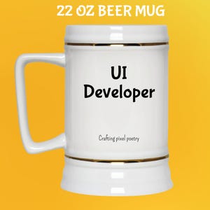 Puede incluir: Taza de cerveza blanca de 650 ml con ribete dorado y asa. La taza tiene las palabras "UI Developer" en negro, con "Crafting pixel poetry" debajo. La taza est&aacute; sobre un fondo amarillo.