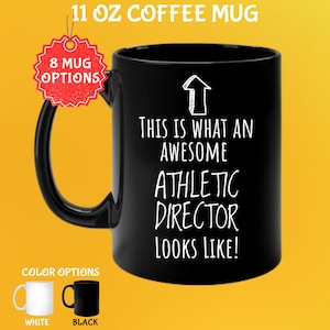 Puede incluir: Taza de café negra de 325 ml con el texto "THIS IS WHAT AN AWESOME ATHLETIC DIRECTOR LOOKS LIKE!" en blanco. La taza tiene un asa negra y un gráfico de flecha blanca. Las opciones de color incluyen tazas blancas y negras.
