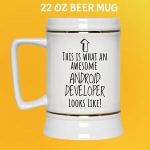 K&ouml;nnte beinhalten: Wei&szlig;er 650 ml Bierkrug mit goldenem Rand und Henkel. Der Krug tr&auml;gt den schwarzen Text "THIS IS WHAT AN AWESOME ANDROID DEVELOPER LOOKS LIKE!". Der Krug steht vor gelbem Hintergrund.