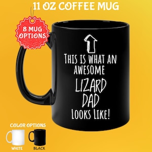 May include: Black 11 oz coffee mug with the text "THIS IS WHAT AN AWESOME LIZARD DAD LOOKS LIKE!" in white. The mug has a black handle and a white arrow graphic. Color options are white and black.