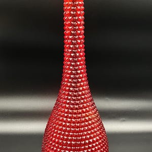 May include: A red glass vase with a textured, diamond pattern. The vase has a long, slender neck and a rounded base. The red colour is vibrant and the texture adds visual interest. The vase is likely for decorative purposes.