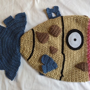 May include: A crocheted fish toy with a brown, beige, and pink body, blue tail fin, and a white eye with a black pupil.