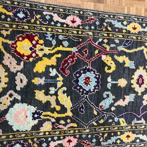 May include: A dark gray rug with a floral pattern in shades of yellow, red, blue, and pink. The rug has a border with a repeating pattern.