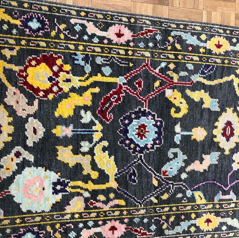 May include: A dark gray rug with a floral pattern in shades of yellow, red, blue, and pink. The rug has a border with a repeating pattern.