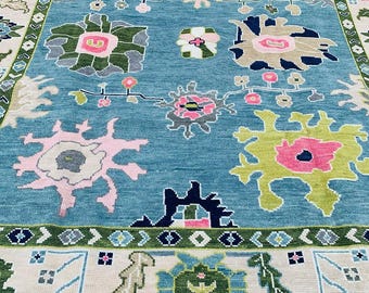 Könnte beinhalten: Ein blauer Teppich mit einem floralen Muster in Rosa-, Grün- und Weißtönen. Der Teppich hat einen Rand mit einem geometrischen Muster.