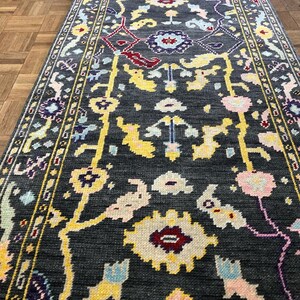 May include: A dark gray rug with a floral pattern in shades of yellow, pink, blue, and purple. The rug has a border with a repeating pattern.