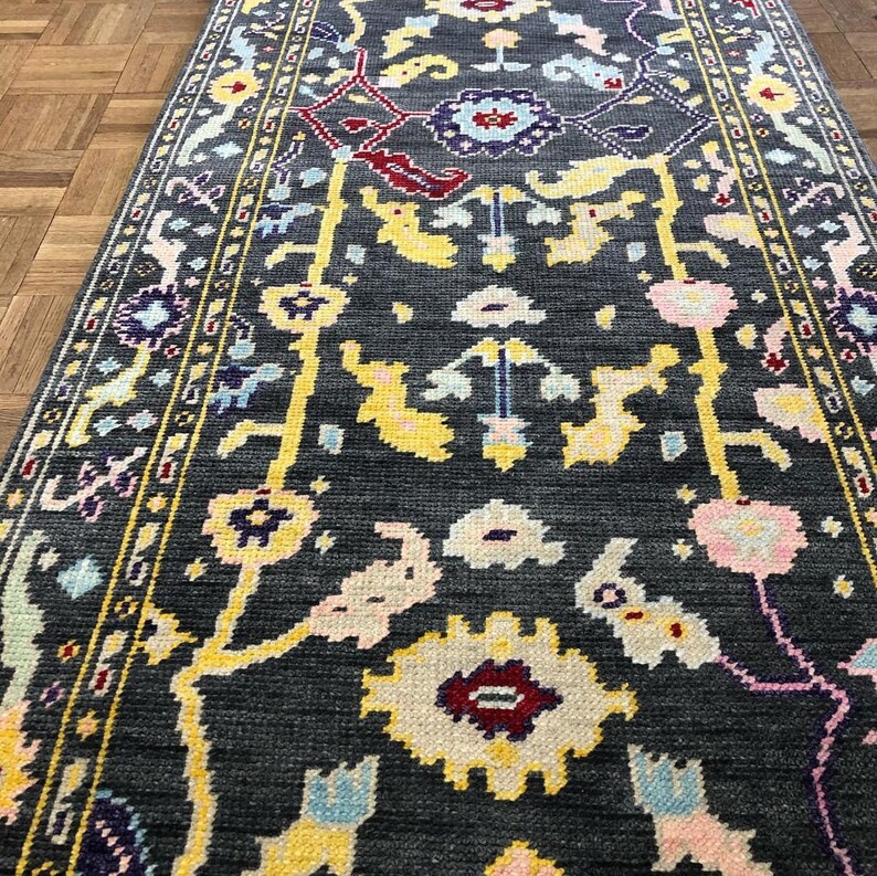 May include: A dark gray rug with a floral pattern in shades of yellow, pink, blue, and purple. The rug has a border with a repeating pattern.