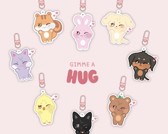 Pode incluir: Uma coleção de pingentes de acrílico com adoráveis animais de desenho animado, incluindo um esquilo, um coelho, um cachorro, um gato e um urso. Cada pingente tem um coração e um fecho. O texto "Gimme a Hug" é exibido no centro, com o texto "Ateez acrylic charms preorder" no topo.