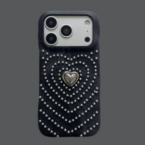 May include: Black denim phone case with a silver heart and studded design. The case features a heart shape made of small silver studs, with a larger silver heart in the center. The case has a dark gray border.