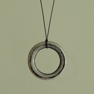 Op de afbeelding: Een eenvoudige, minimalistische ketting met een witte keramische ring als hanger. De ring is dik en heeft een zwarte lijn rond de rand.