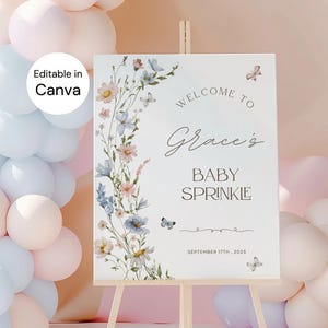May include: A white baby sprinkle welcome sign on a wooden easel, decorated with watercolor flowers and butterflies. The sign reads "Welcome to Grace's Baby Sprinkle" and includes the date September 17th, 2025. Balloons in pastel colors are in the background.