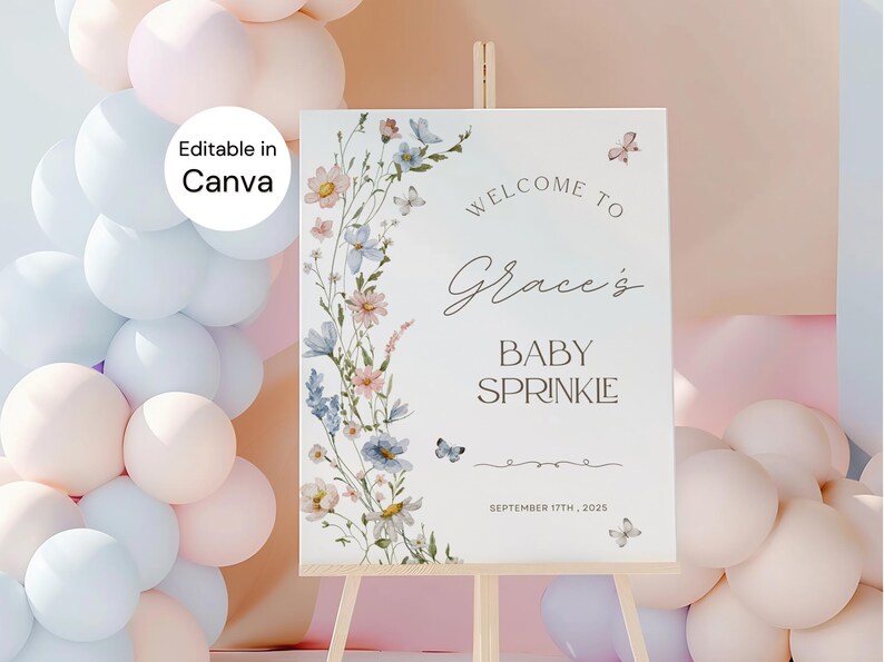 May include: A white baby sprinkle welcome sign on a wooden easel, decorated with watercolor flowers and butterflies. The sign reads "Welcome to Grace's Baby Sprinkle" and includes the date September 17th, 2025. Balloons in pastel colors are in the background.