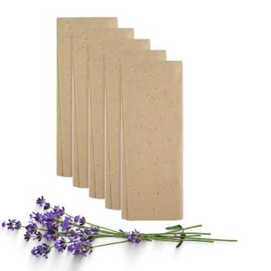 May include: Six rectangular sheets of light brown gift wrap with gold flecks. A sprig of fresh lavender with purple flowers and green stems is placed in front of the paper, creating a natural, floral accent.