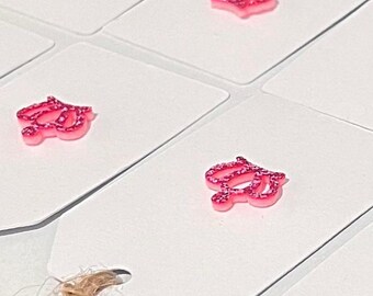 May include: Close-up of white gift tags with a pink glittery cursive letter design. The tags are arranged on a white surface, with a natural twine string visible. The pink design adds a touch of sparkle.