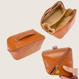 May include: Three brown cosmetic bags in different views. One bag is closed with a handle, another is open showing interior compartments, and the third is partially open with a diagonal zip and a gold-coloured charm.