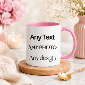 May include: A white ceramic mug with a pink interior and a pink handle. The front of the mug features black text that reads Any Text, ANY PHOTO, and Any design. The mug is positioned on a round wooden coaster.