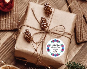 Könnte beinhalten: Ein Geschenk in braunes Papier verpackt, mit Bindfaden und Tannenzapfen verziert. Ein runder Aufkleber mit "Thank You" und Namen ist angebracht. Das Geschenk liegt auf einer Holzoberfläche mit Weihnachtsdekorationen.