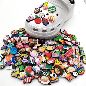 May include: A large collection of colorful shoe charms featuring various designs, including animals, food, emojis, and phrases like "Hey Good" and "Good Vibes".