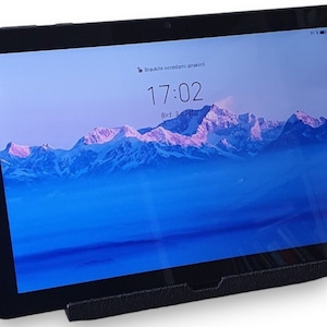 以下が含まれることがあります： 黒いタブレットコンピュータ。山脈の壁紙と画面に表示された時刻17:02。タブレットは黒いスタンドの上に置かれています。