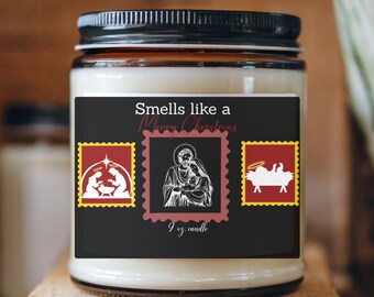May include: A glass jar candle with a black lid and a label that reads "Smells like a Merry Christmas." The label features three postage stamp-style images with religious themes. The candle is 9 oz.