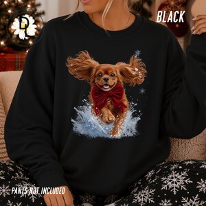 May include: A black crewneck sweatshirt featuring a graphic of a brown spaniel dog with long ears wearing a large red velvet bow, jumping through a splash of water with snowflakes, with the text BLACK and PANTS NOT INCLUDED visible.