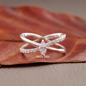 May include: A silver ring featuring a marquise-shaped diamond and a criss-cross design. The band is set with smaller diamonds. The image includes the text "Jewelry Choice".