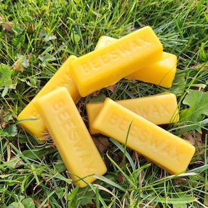 May include: Several yellow beeswax blocks with the word "Beeswax" printed on them. The blocks are arranged on a bed of green grass.