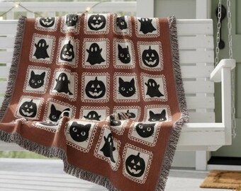 May include: A brown and black Halloween-themed throw blanket draped over a white porch swing. The blanket features repeating squares with black cat faces, jack-o'-lanterns, and ghosts. The porch is decorated with fall-themed decor.