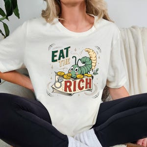 Camiseta gráfica "Eat The Rich", tipografía retro de los 70, diseño rebelde y divertido, estampado de caricatura caprichoso, regalo atrevido para amigos.