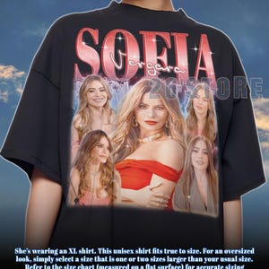 Puede incluir: Camiseta unisex negra con un collage de imágenes de Sofia Vergara y el nombre "SOFIA VERGARA" en rosa brillante. También es visible el texto "26 STORE". La descripción de la camiseta está en la parte inferior.