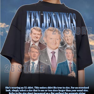 May include: Black unisex t-shirt featuring a graphic of Ken Jennings with the text "KEN JENNINGS" in blue. The shirt has a crew neck and short sleeves. The shirt is a relaxed fit.