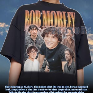 Puede incluir: Camiseta unisex negra con un collage de imágenes y el nombre "BOB MORLEY" en un estilo vintage. La camiseta tiene cuello redondo y mangas cortas. El diseño incluye múltiples imágenes de una persona. El texto "26TORE" también es visible.