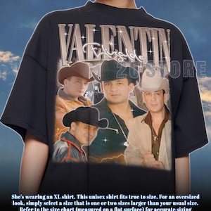 May include: Black unisex t-shirt featuring a graphic of four men in cowboy hats with the text "VALENTIN Elizalde" in a vintage style. The shirt has short sleeves and a crew neck. The text "26 STORE" is also visible.