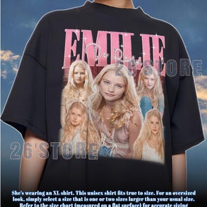 May include: Black unisex t-shirt featuring a pink graphic with the name "EMILIE" and a photo collage of a blonde woman. The shirt has a crew neck and short sleeves. The text "26'STORE" is also visible.
