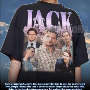 以下が含まれることがあります： 黒色のユニセックスTシャツ。紫色のスタイリッシュなフォントで「JACK」という名前と画像のコラージュが特徴です。シャツには「26'STORE」の文字とサイズガイドが含まれています。