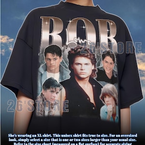 May include: Dark grey unisex t-shirt with a collage of vintage movie stars. The word "ROB" is printed in a metallic silver font. The text "26'STORE" is also visible. The shirt is a unisex fit.