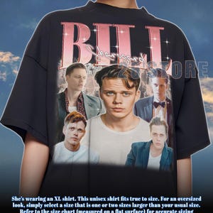 May include: Black unisex t-shirt featuring a collage of images and the name "BILL Skarsgard" in pink. The shirt has a crew neck and short sleeves. The text at the bottom says, "She's wearing an XL shirt. This unisex shirt fits true to size."