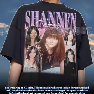 Könnte beinhalten: Schwarzes Unisex-T-Shirt mit einer Collage von Shannen Doherty-Bildern und dem Namen "SHANNEN" in lila Schrift. Das Shirt enthält auch den Text "268 STORE" und Größeninformationen.