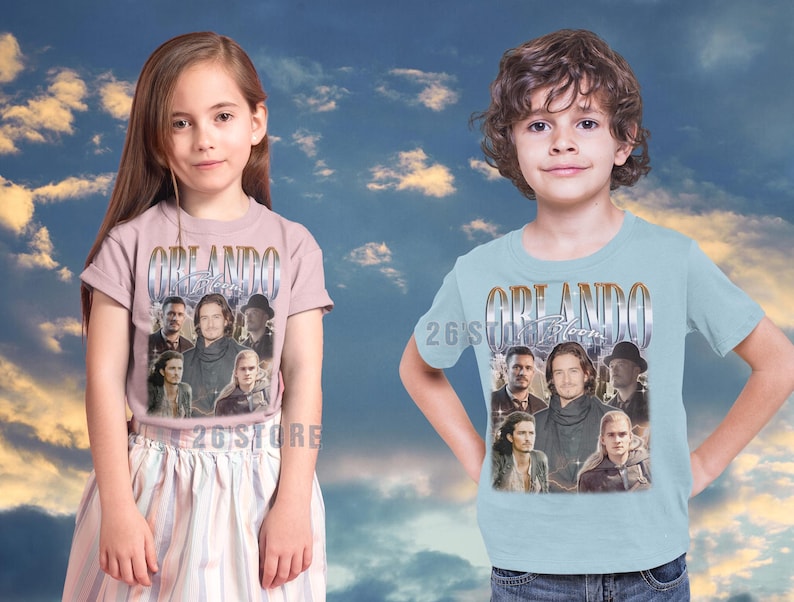 May include: Two children wearing t-shirts with the word "Orlando" in a vintage style font. The shirts feature a collage of images of people. The girl is wearing a pink shirt and the boy is wearing a light blue shirt. The text "26'S STORE" is at the bottom.
