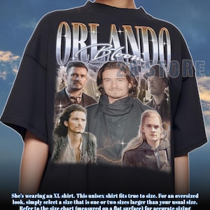 May include: Black unisex t-shirt featuring a collage of Orlando Bloom images with the name "ORLANDO Bloom" in a silver, vintage-style font. The shirt has a crew neck and short sleeves. The text "20STORE" is also visible.