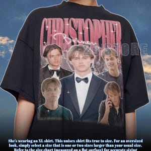 Könnte beinhalten: Schwarzes Unisex-T-Shirt mit einer Collage von Bildern und dem Text "CHRISTOPHER B." in rosa, im Retro-Stil. Das T-Shirt hat einen Rundhalsausschnitt und kurze Ärmel. Der Text am unteren Bildrand ist nicht enthalten.